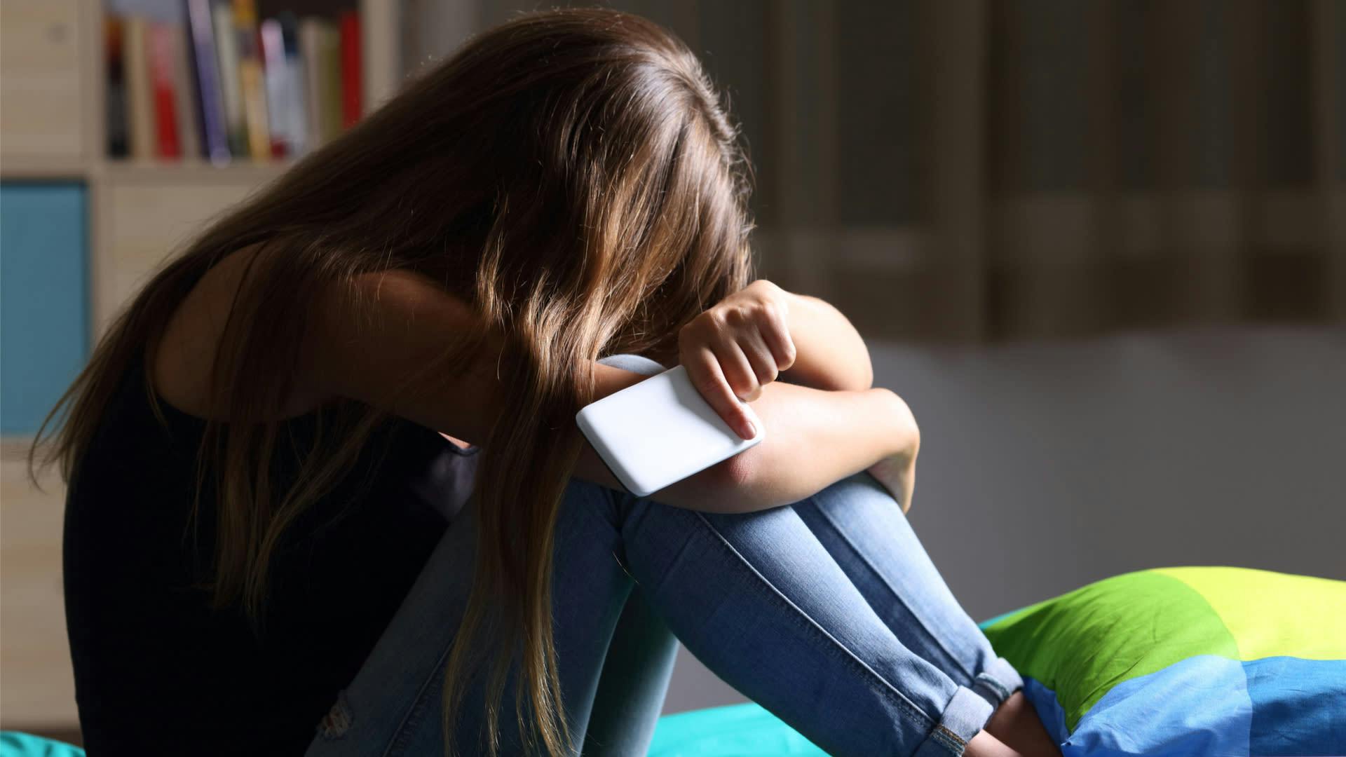 Girl is upset with mobile phone in her hand after suffering from cyber bullying